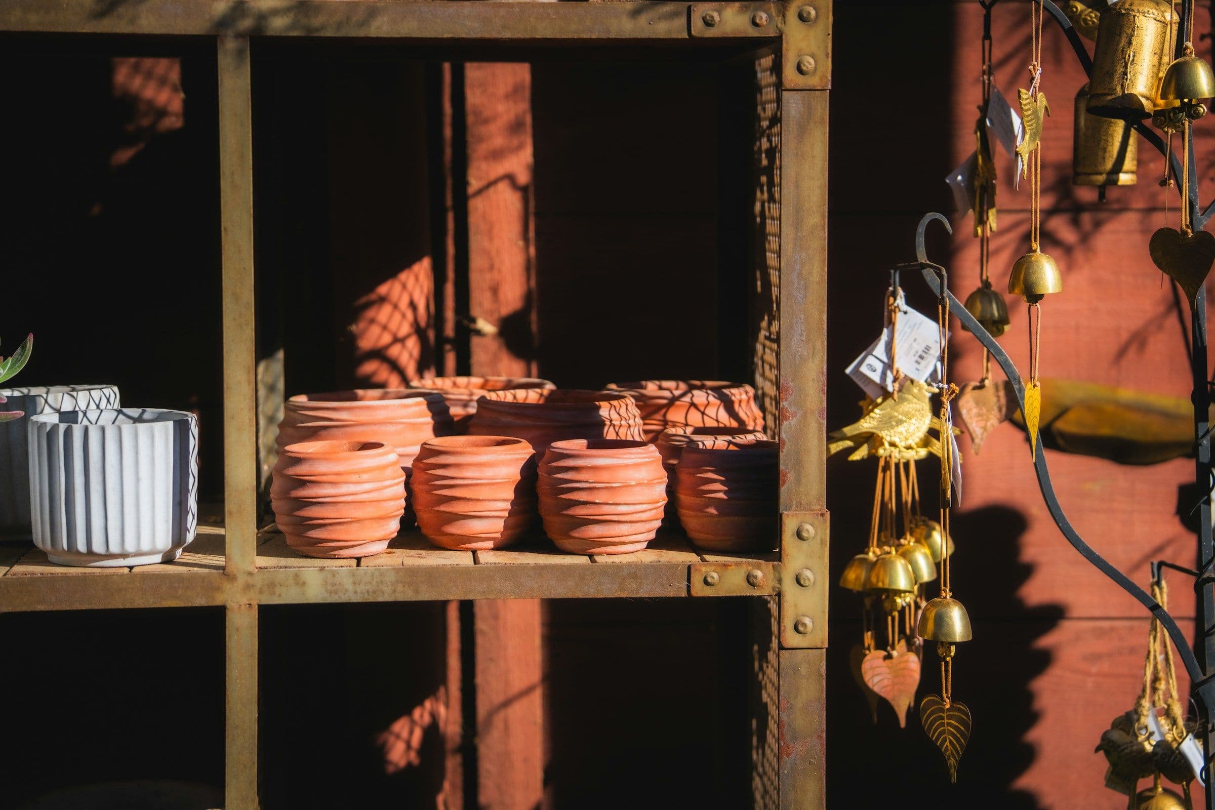 Rows of warm terracotta pots beside pale glazed ceramic planters on a metal shelf